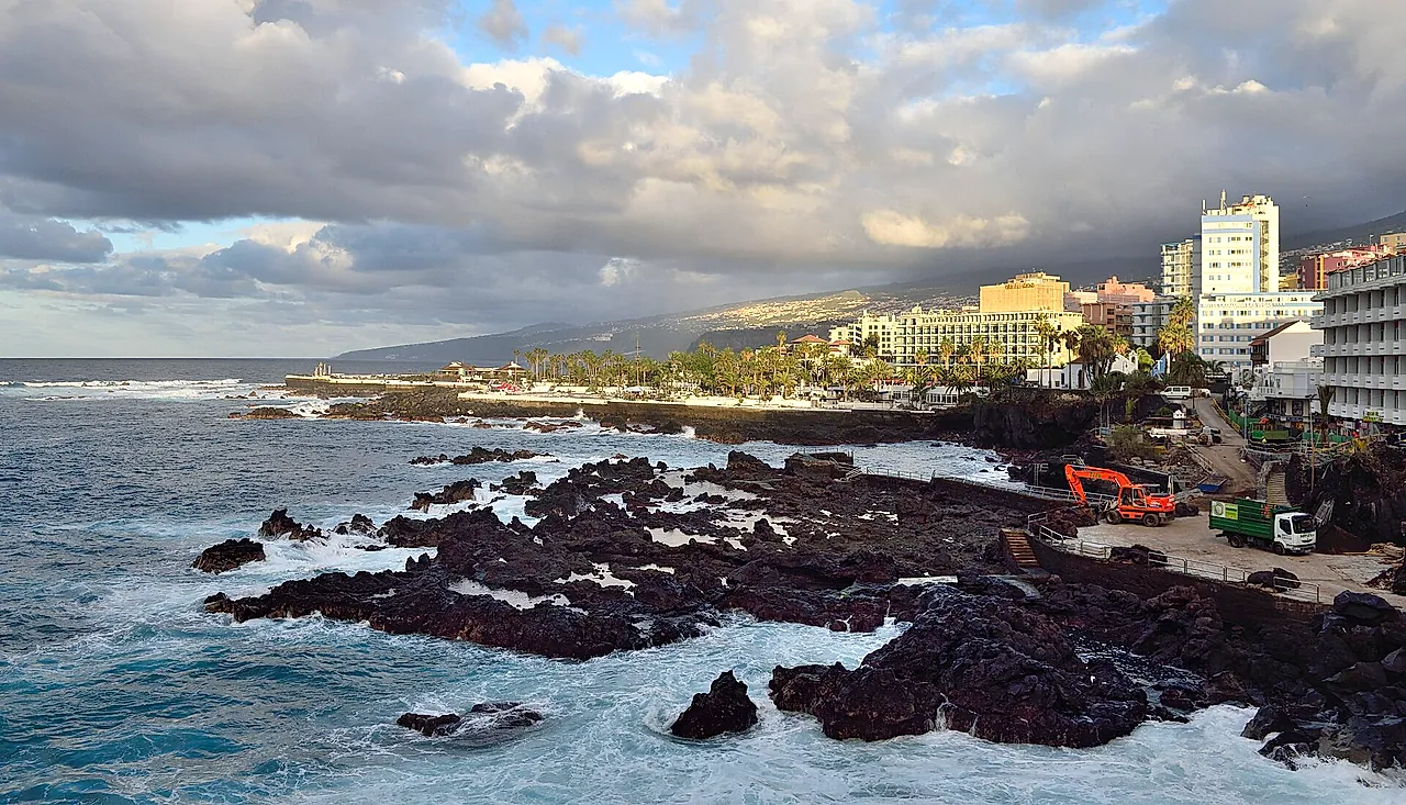 Black volcanic rocks and waves on the coast of Puerto de la Cruz in the afternoon light, with the town behind