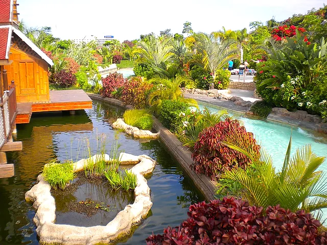 A winding lazy river canal lined with tropical plants and wooden Thai-style houses at Siam Park